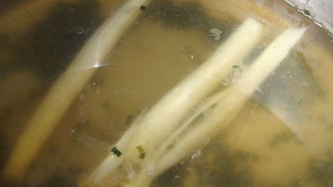 Spargelstangen liegen in einer klaren Brühe, während sie darin kochen und Aromen für Reis abgeben.