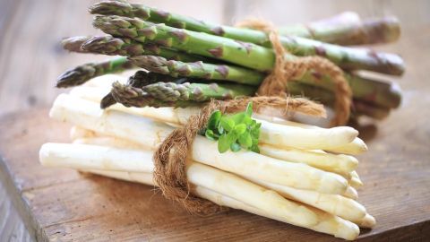 Grüner und weißer Spargel liegen gebündelt auf einem Holztisch, dekoriert mit frischem Kraut.