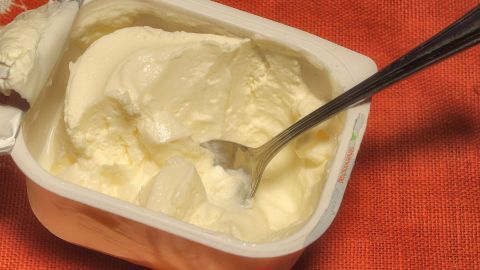 Eine Schale Quark steht auf einem roten Tuch, während ein Löffel dabei ist, um den Quark zu servieren.