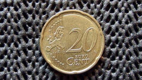 Eine 20-Cent-Münze liegt auf einer strukturierten, dunklen Unterlage. Es wird auf den Einkaufswagen-Bonus angespielt.