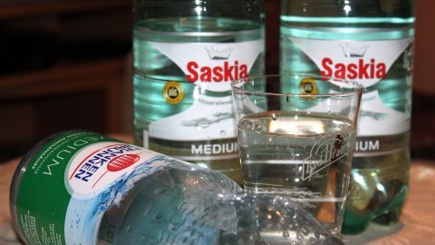 Zwei Wasserflaschen stehen neben einem Glas mit Wasser, während eine Flasche schräg liegt; perfekt für Sauna gegen Kater.