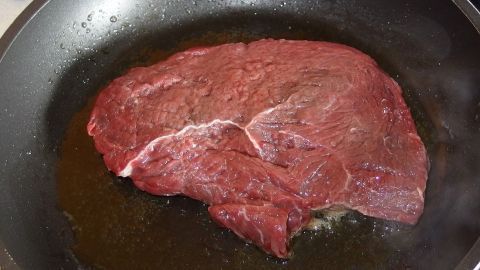 Ein großes Stück Fleisch liegt in einer Pfanne, während es angebraten wird, um ein saftiges Steak zuzubereiten.