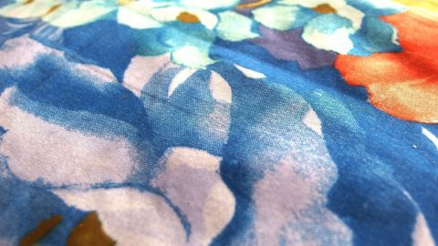 Mit Sprudelwasser kann man prima Fruchtsaftflecken entfernen. Bunte, blumige Textiloberfläche mit Saftflecken, die durch Sprudelwasser behandelt wird, um Verfärbungen zu entfernen.