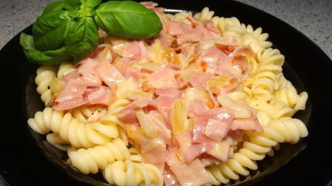 Ein Teller Nudeln mit Schinken-Sahne-Soße ist appetitlich angerichtet, garniert mit frischem Basilikum auf einem dunklen Untergrund.