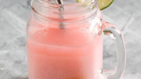 Ein Glas Joghurtdrink mit einem Strohhalm steht auf einem grauen Hintergrund. Limettenscheiben liegen daneben.