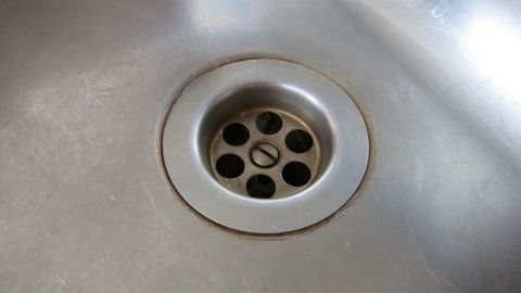 Ein Spülbecken mit verfärbtem Edelstahl um den Abfluss, der schmutzig wirkt und gebrauchsspuren aufweist.