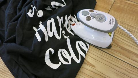 T-Shirt-Aufdruck mit dem Bügeleisen verschmiert? So kann man manchmal noch das eine oder andere Lieblingsteil retten. Ein Bügeleisen liegt auf einem schwarz bedruckten T-Shirt, das durch die Anwendung verschmiert aussieht.