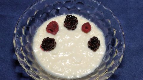 In einer klaren Schüssel liegt Magerquark, garniert mit Himbeeren und Brombeeren, auf einem blauen Tisch.