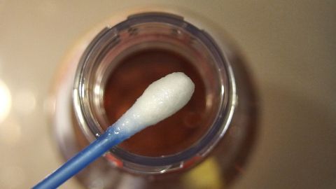 Ein Q-Tip taucht in eine Flasche mit Apfelessig, um Herpes mit der Flüssigkeit zu behandeln.