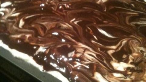 Ein Kuchen mit einer glatten, schokoladigen Glasur und cremigen Schichten wird in der Küche zubereitet.