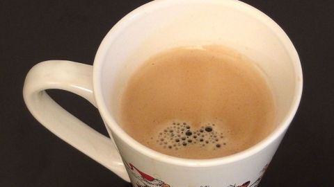 Ein weißer Becher mit braunem Kaffee schwimmt auf einer dunklen Oberfläche, möglicherweise in einem gemütlichen Raum.