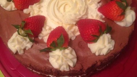 Eine Torte mit Schokoladenmousse und Vanillecreme, dekoriert mit frischen Erdbeeren und Sahne, auf einem rosa Teller.