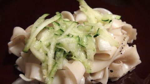 Ein Nudelsalat mit grüner Gurke liegt auf einem dunklen Teller und zeigt frische, geschnittene Gurkenstreifen auf den Nudeln.