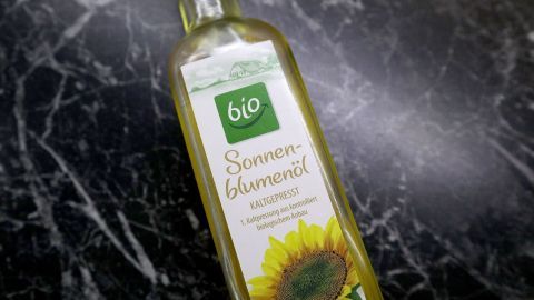 Eine Flasche Sonnenblumenöl steht auf einer dunklen, marmorierten Oberfläche und zeigt auf das etikettierte Bio-Produkt.