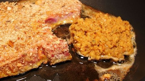 Ein Schnitzel brät in einer Pfanne, während daneben die restliche Panade in Öl knusprig wird.