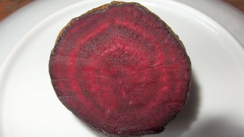 Eine rote Bete liegt auf einem weißen Teller, bereit zum Färben von Shirts. Ihre leuchtend rote Farbe zeigt die natürliche Färbemethode.