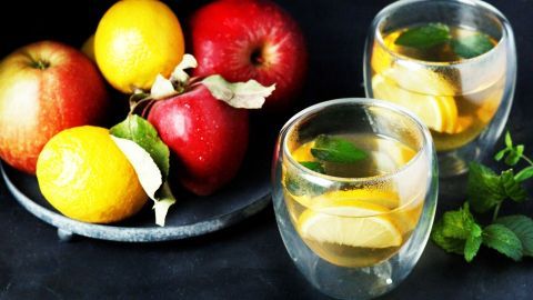 Frische Äpfel und Zitronen liegen neben zwei Gläsern mit einem Super Vitamin-Drink, der mit Minze garniert ist.