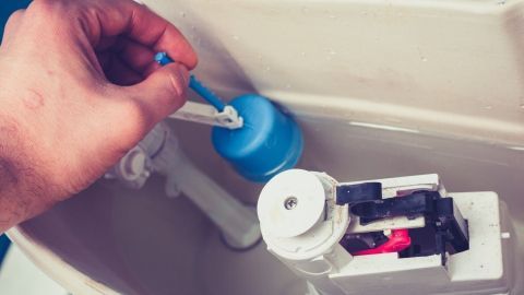 Ein Hand mit einem blauen Schwimmer fixiert den Toilettenspülkasten, um das Problem mit dem Wasser zu beheben.