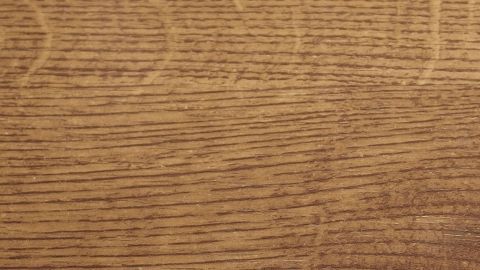 Eine hölzerne Oberfläche zeigt feine, dunkle Holzmaserungen in einem warmen Braunton, mit leichten, unregelmäßigen Flecken.
