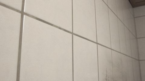 Weiße Fliesen zeigen Kalkablagerungen und Schmutz, stehen in einem Badezimmer mit Holzdecke und leichtem Licht.