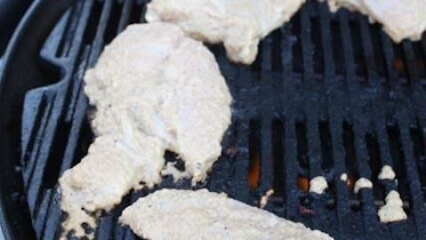 Hähnchenstücke brutzeln auf einem Grill, in honiggelber Marinade gehüllt, während Rauch durch die Rillen aufsteigt.