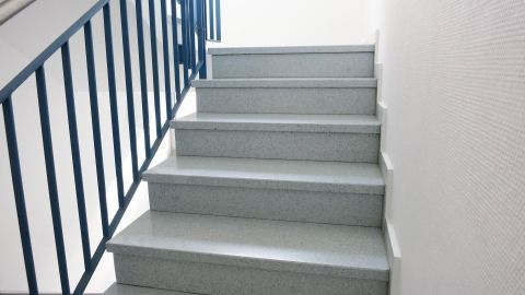 Beim Treppe putzen, nur wischen und nicht fegen, weil beim Fegen der (Fein-)Staub aufwirbelt wird. Eine saubere Treppe wird von unten nach oben betrachtet, umgeben von hellen Wänden und einem Geländer.
