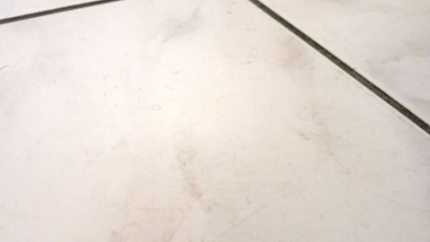Boden reinigen mit einem kleinen Schuss Fensterreinigungskonzentrat für Autowaschanlagen im Wischwasser. Ein schmutziger Boden mit Fliesen zeigt verschiedene Flecken. Das Bild vermittelt den Bedarf an Bodenreinigung mit Fensterreinigungskonzentrat.