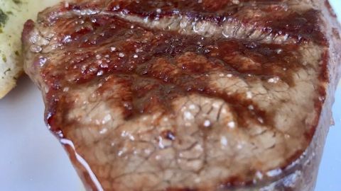Saftiges, gegrilltes Steak auf einem weißen Teller, umgeben von buntem Salat und einer Beilage, appetitlich angerichtet.