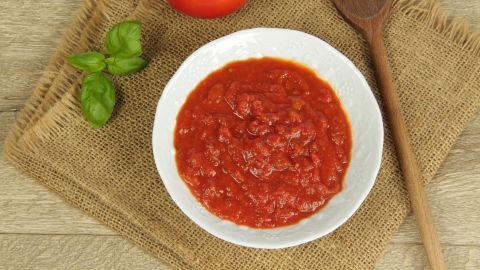 Wenn Ihr mal wieder Lust auf Spaghetthi mit Tomatensoße habt und kein Tomatenmark zur Hand habt, könnt Ihr auch 2-3 Tomaten nehmen diese pürieren oder einfach kochen... Eine Schüssel mit Tomatenmark steht auf einem rustikalen Untergrund, umgeben von einer Tomate und frischem Basilikum.