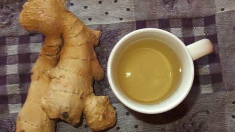 Ein Stück frischer Ingwer liegt neben einer Tasse Ingwertee auf einem gemusterten Tisch, der die Verdauung fördern soll.