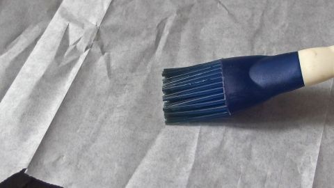 Das Backpapier ist ausgegangen? Einfach Butterbrotpapier verwenden. Ein Pinsel liegt auf Butterbrotpapier, während er bereit ist, die Oberfläche zu bestreichen.