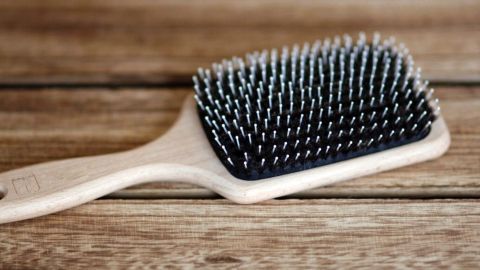 Eine Holzhaarbürste liegt auf einer rustikalen Holztischoberfläche und wartet darauf, mit Shampoo gereinigt zu werden.