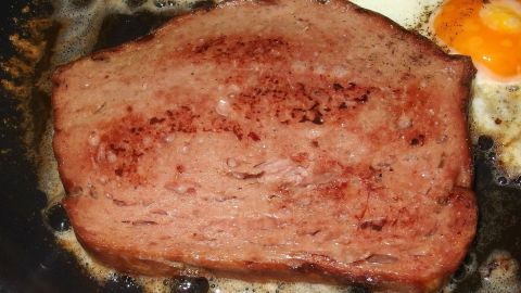 Ein frisch gebratener, original bayrischer Leberkäse liegt in einer Pfanne, umgeben von zerlaufenem Fett und einem Spiegelei.