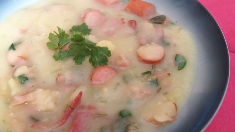 In einer Schüssel liegt eine cremige Kartoffelsuppe, die mit Gemüse und Kräutern garniert ist. Sie ist appetitlich angerichtet.