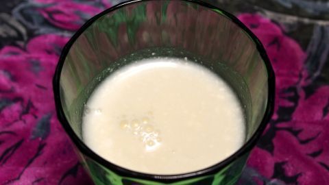 Ein Glas Buttermilch steht auf einem bunten, blühenden Hintergrund und vermittelt eine erfrischende Wirkung bei Regelschmerzen.