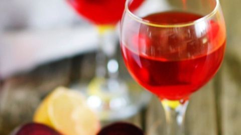Zwei Gläser Rote Beete Wein stehen auf einem Holztablett, während geschnittene Rote Beete und Zitrone daneben liegen.