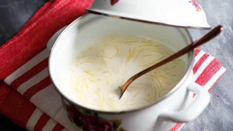 Eine Schüssel Milchnudelsuppe mit einem Löffel steht auf einem roten Geschirrtuch, bereit zum Servieren als Dessert oder Hauptmahlzeit.