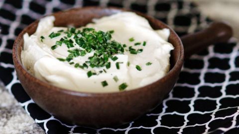 Eine Schüssel Labneh, verziert mit frischem Schnittlauch, steht auf einem gemusterten Tuch in einer hellen Umgebung.