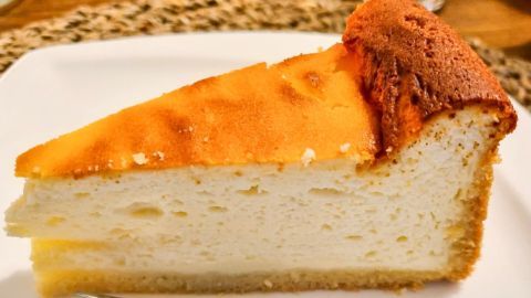 Ein Stück Quarktorte liegt auf einem weißen Teller, während eine Gabel daneben bereitliegt, um es zu genießen.