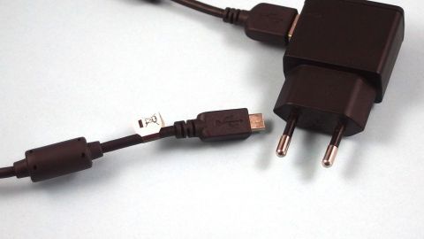 Ein schwarzer Handy-Ladeadapter mit Kabel liegt auf einer hellblauen Oberfläche und ist bereit, Strom zu sparen.
