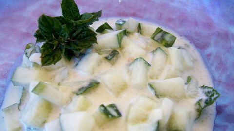 Eine Schüssel Tzatziki mit gewürfelten Gurken und frischer Minze, bereit zum Servieren in einer hellen Umgebung.