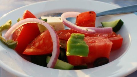 Frischer griechischer Salat mit Tomaten, Gurken, Zwiebeln und Feta auf einem weißen Teller bei warmem Licht.