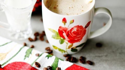 Eine dekorative Tasse mit russischem Kaffee steht auf einem Tisch, umgeben von Kaffeebohnen und einer kleinen Milchkanne.