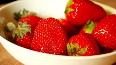 Frische Erdbeeren liegen in einer weißen Schale auf einem holzfarbenen Tisch, bereit für den Genuss gegen Pickel.