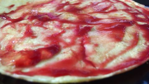 Die Marmelade mit Balsamico-Essig wird auf einem dünnen Pfannkuchen drapiert, umgeben von einem dunklen Hintergrund.