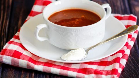 Ein weißes Schüssels mit scharfer Suppe, dekoriert mit einem Löffel Sauerrahm, steht auf einem karierten Tuch.