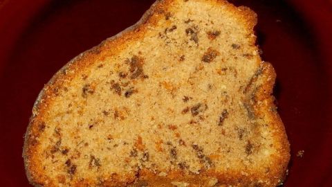 Ein Stück Nusskuchen mit Schokoladenstückchen liegt auf einem roten Teller, umgeben von einer einladenden Küchenszene.