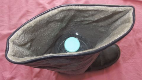 Ein Stiefel liegt auf einem roten Untergrund, während eine Flasche darin steht, um ihm Struktur zu verleihen.