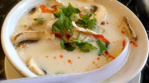 Eine weiße Schüssel mit Currysuppe enthält frische Kräuter, Hähnchen und Chili, umgeben von einem elegantem Tisch.