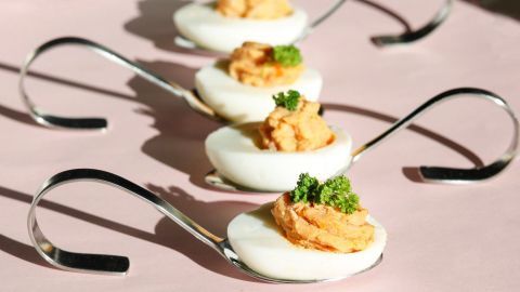 Gefüllte Eier mit Thunfisch sind auf silbernen Löffeln angerichtet, umgeben von einem rosa Hintergrund.